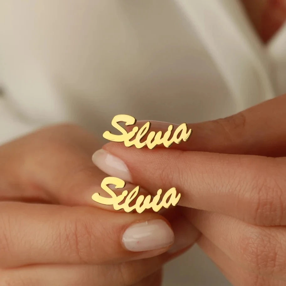 Gold 'Silvia' earrings on a person's hand with a blurred background